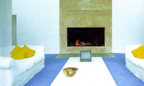 A beautiful white living area set off by the spare and cool granite fireplace and accented with warm lemon yellow and icy blue